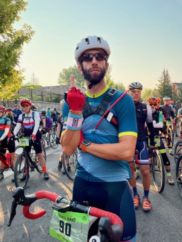 Man in bike kit standing over his bike and flipping the bird