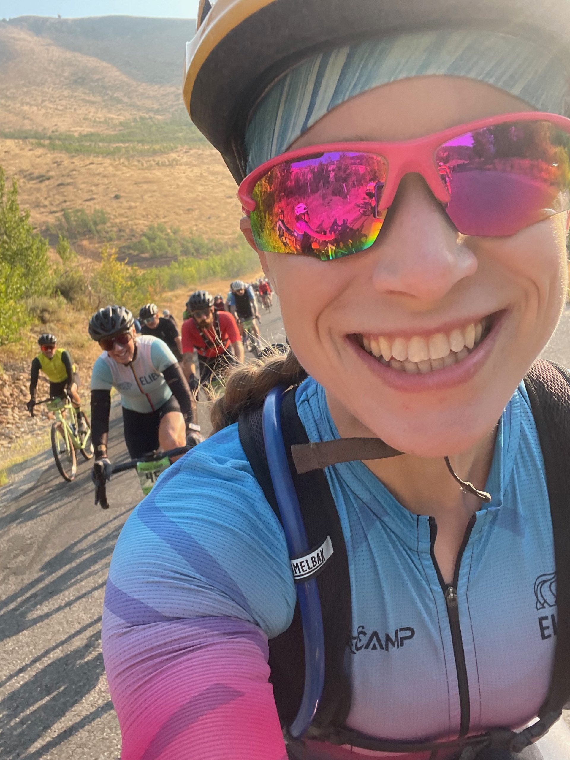 Selfie of woman on a bike with a line of riders behind her in early morning light
